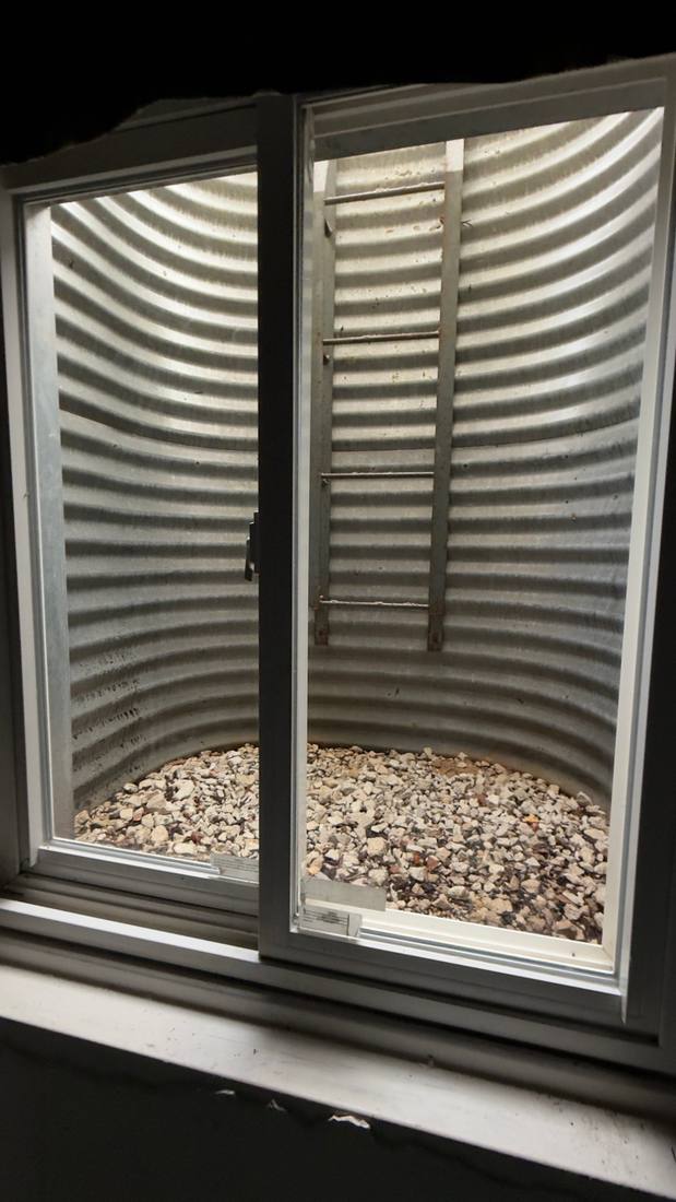 Clean metal window well with gravel, seen from the basement